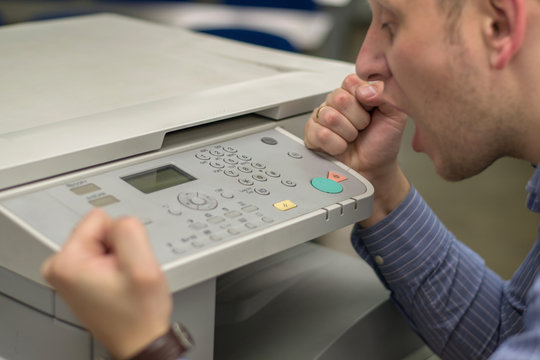 Angry Young Business Man Beats His Fist On A Multifunction Printer Or Copier