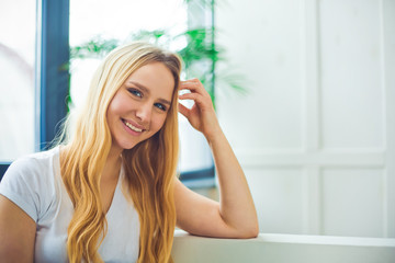 Fototapeta premium Close up Portrait of a beautiful smiling young blond woman sitting at home on a sofa and resting or relaxing.