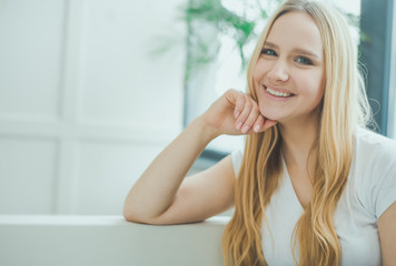 Close up Portrait of a beautiful smiling young blond woman sitting at home on a sofa and resting or relaxing.