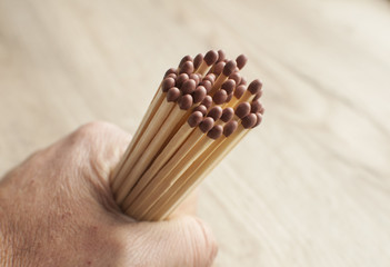 A bunch of wooden matchsticks held in human wrist closeup on wooden background