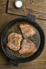 three fried pork steaks in a frying pan