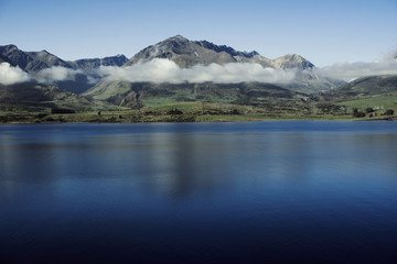 Paisaje de montañas con picos nevados y nubes. Las montañas se reflejan en un lago. Escena diurna, cielo azul y despejado. Nueva Zelanda.
