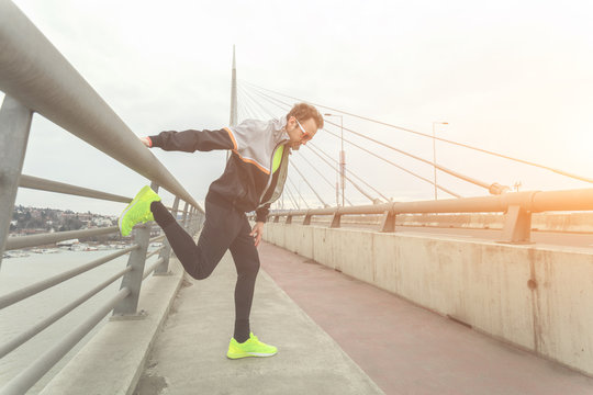 Urban Jogger Stretching On A Bridge Above The River.