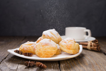 Delicious eclairs sprinkled with icing sugar, stand on a wooden table. Copy spase.