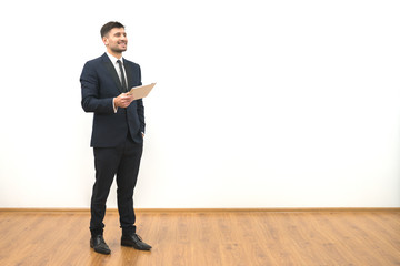 The happy man with a tablet standing on the white wall background