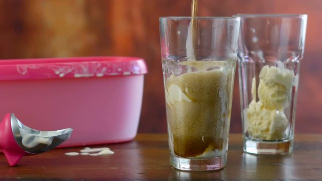 Preparing black cow cola ice cream soda floats against rustic wood background.