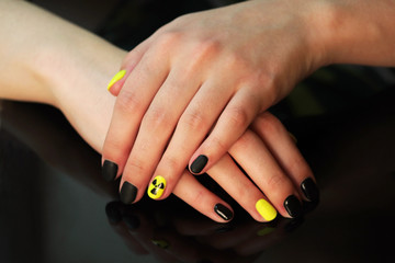 Obraz na płótnie Canvas beautiful black-and-yellow manicure with shellac varnish in the form of a sign of radioactive danger. hands of the girl on a black shiny background
