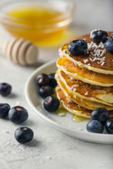 Pancakes with blueberries and honey on a plate on white background