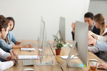 Office employees working on pc computers talking sharing desk in co-working, diverse business people using desktops sitting together, team workplace, teamwork concept, close up of table with monitors