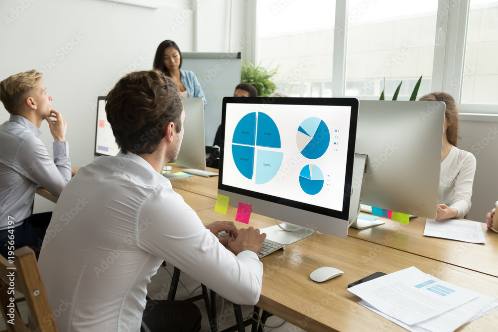 Poster employee analyzing statistics data charts on computer screen working in office with multiracial team