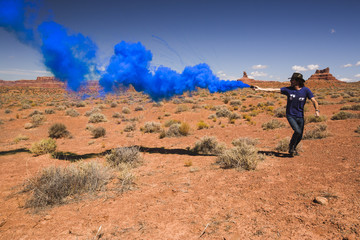 Man runs playfully  through desert holding blue smoke bomb