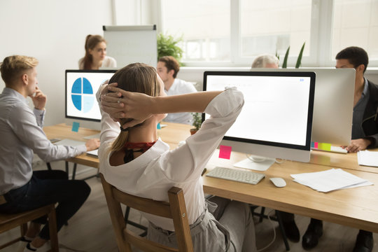 Rear view at businesswoman holding hands behind head resting after finishing work on computer in multiracial office, company manager employee relaxing or thinking taking short break at workplace