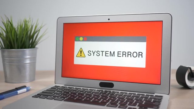 System error message warning showing on a laptop computer screen sitting on a desk. Camera is slowly turning around the computer.