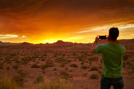 man taking photo with smartphone of very colorful sunset in nevada desert