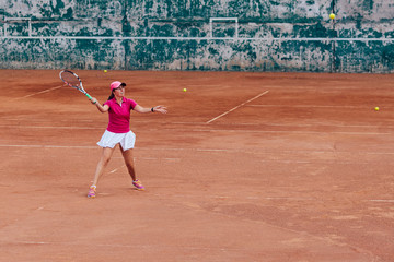 Tennis player. Active sportive woman playing tennis, ready for receive a ball, dressed in pink t-shirt, cap and white skirt. Side view.