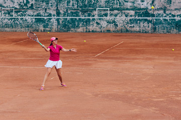 Obraz premium Tennis player. Active sportive woman playing tennis, ready for receive a ball, dressed in pink t-shirt, cap and white skirt. Side view.