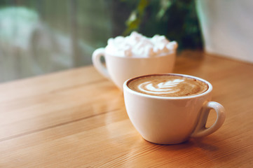 Two cups of cappuccino with latte art and marshmallow on wooden background. Beautiful foam, greenery ceramic cups, stylish toning, place for text.