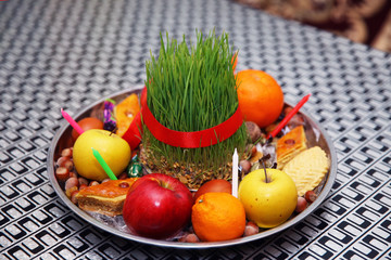 Novruz tray plate with Azerbaijan national pastry pakhlava and shekerbura purple silk scarf . Semeni on vintage plate decorated with red cord on national style table cloth . Apple, candle, nuts .