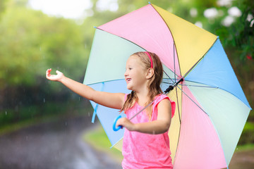Kid with umbrella playing in summer rain.