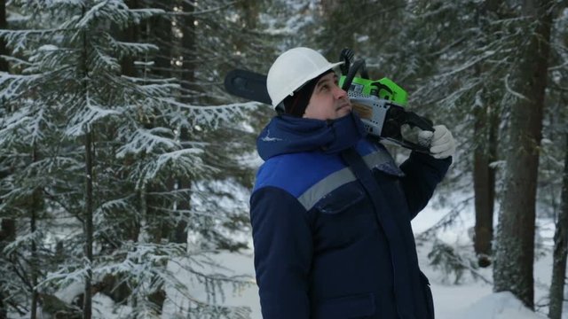 Worker with chainsaw on shoulder looking around in winter forest