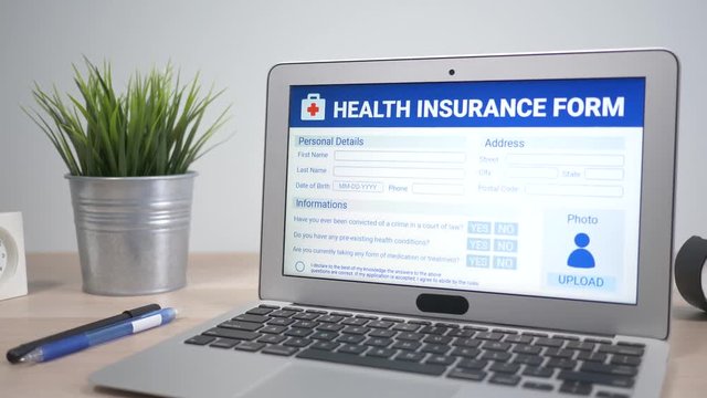 Online health insurance application form showing on a laptop computer screen sitting on a desk. Camera is slowly turning around the computer.