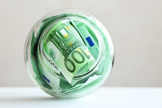 Euro banknotes in a glass jar on a grey background