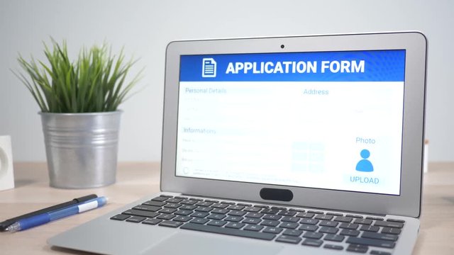 Online application form showing on a laptop computer screen sitting on a desk. Camera is slowly turning around the computer.