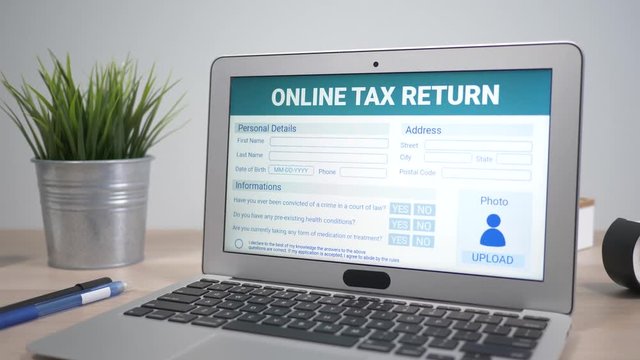 Tax return form showing on a laptop computer screen sitting on a desk. Camera is slowly turning around the computer.