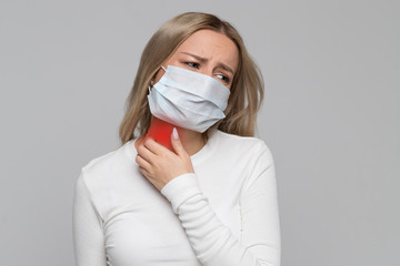 Studio portrait of unhealthy woman in medical face mask scratching her neck colored in red, isolated on grey background. Symptoms of animal or seasonal allergy