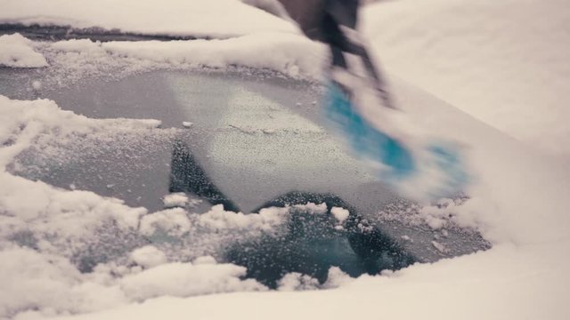 A young man cleans the window of the car from the snow.