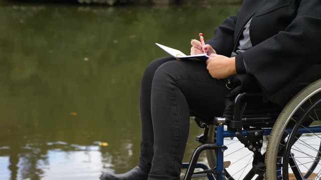 woman on wheelchairs writes a love letter near the lake