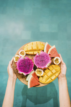 Crop hands with board of tropical fruit