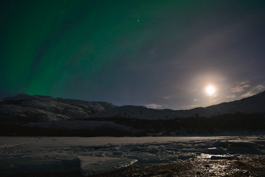 Night winter landscape with Moon and aurora borealis on the sky. Barents sea coastline, Kola peninsula, Russia.