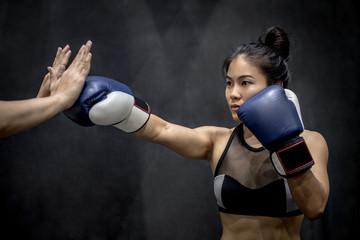 Naklejka na ściany i meble Young Asian woman boxer with blue boxing gloves punching to her trainer’s hand in training gym, Martial arts on black background