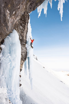 Man climbing on frozen cascade with icicles hanging from above