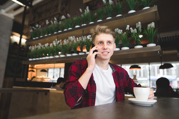 A student talks by phone in the cafe and smiles. A young man drinks coffee and talks over the phone