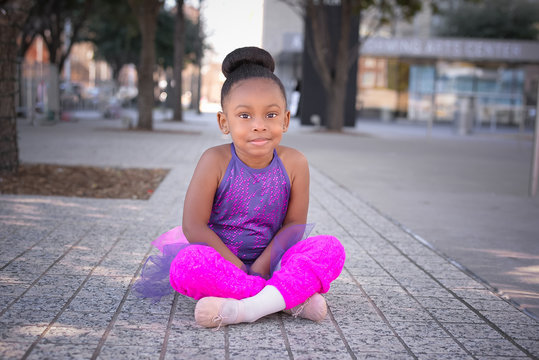 Little girl wearing tutu and sitting on sidewalk