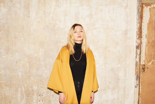 Sensual blonde girl in yellow coat over shabby wall.