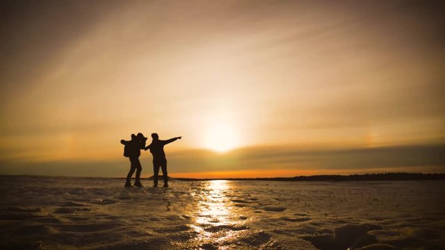 The Silhouette of two men walking on the sunrise with Backpacks. Tourists take photos while traveling. Travel concept.