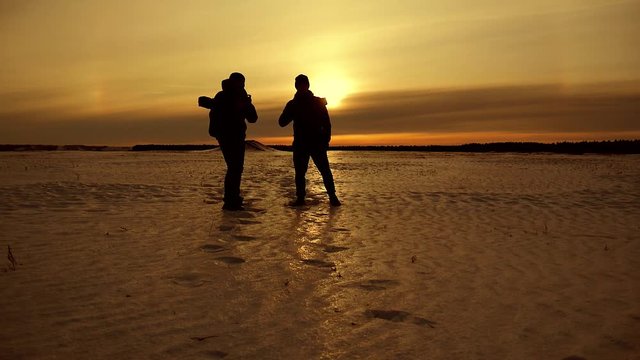 The Silhouette of two men walking on the sunrise with Backpacks. Tourists take photos while traveling. Travel concept.