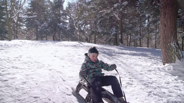 Boy sitting on a sledge and going down on the hill
