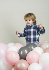 Fototapeta na wymiar Little boy jumps in pink balloons. Funny kid play on his own on white background. Pink, white and gray balloons for celebration. Cute boy wearing blue shirt and grey jeans. Clothes for children