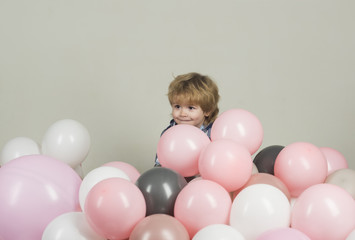 Fototapeta na wymiar Surprise. Hide and seek for children surrounded with balloons. Little kid hides in colourful balloons. Child with cute smile hides in pink, grey and white balloons. Decorations for children's Birthday