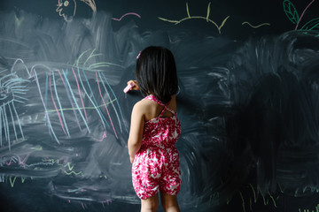 Toddler girl drawing on blackboard wall