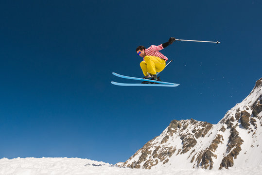Side view of male skier jumping off snow-capped cliff
