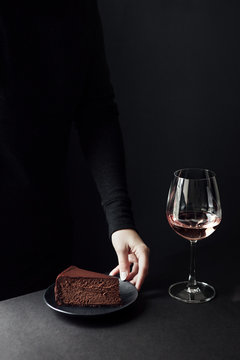 Woman Holding Chocolate Cheesecake And Wine Against Black Background