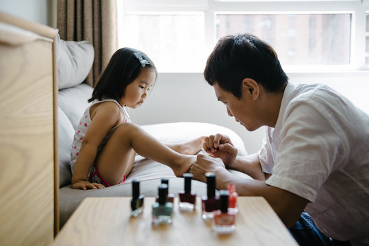 Father painting daughter toenails with fingernail polish