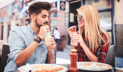 Beautiful young couple sitting in the cafe and eating pizza. Consumerism, food, lifestyle concept