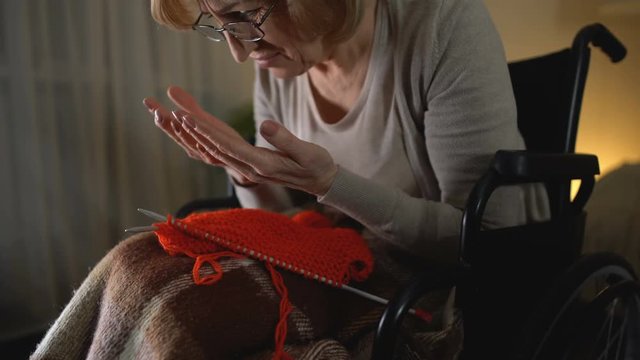Retire lady in despair looking at shaking hands, crying helplessly in wheelchair