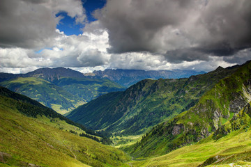 Sunny alpine meadows and forests in valleys of Karnische Alpen with ridges of Gailtaler Alpen / Lienzer Dolomiten in white cumulus clouds in background, Untertilliach Lesachtal Osttirol Austria Europe